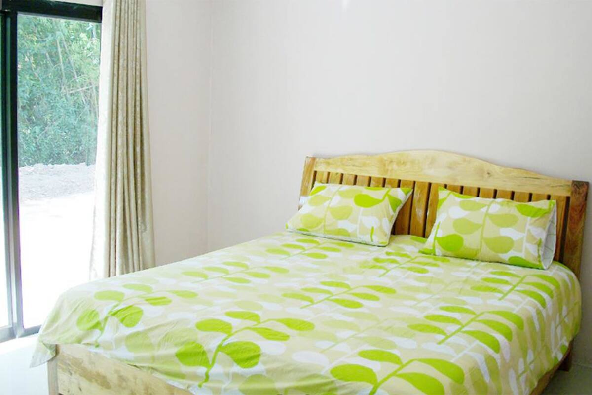 A bedroom with a wooden headboard, two pillows with a leaf pattern, and a bed with a leaf-patterned bedspread.