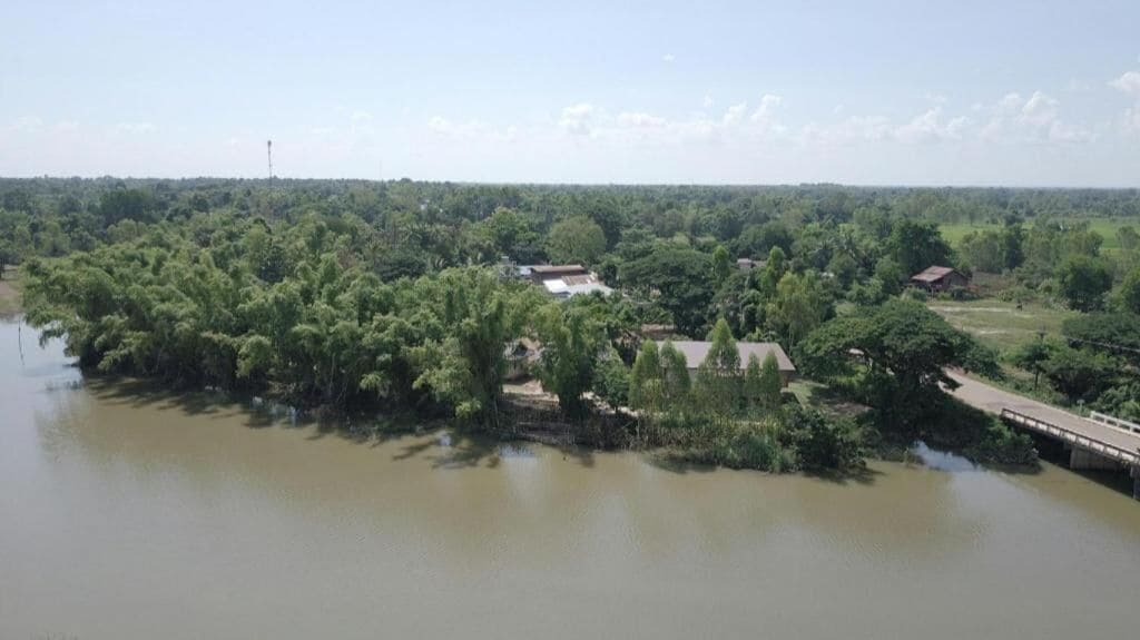 A river with a bridge, surrounded by dense greenery and scattered buildings.