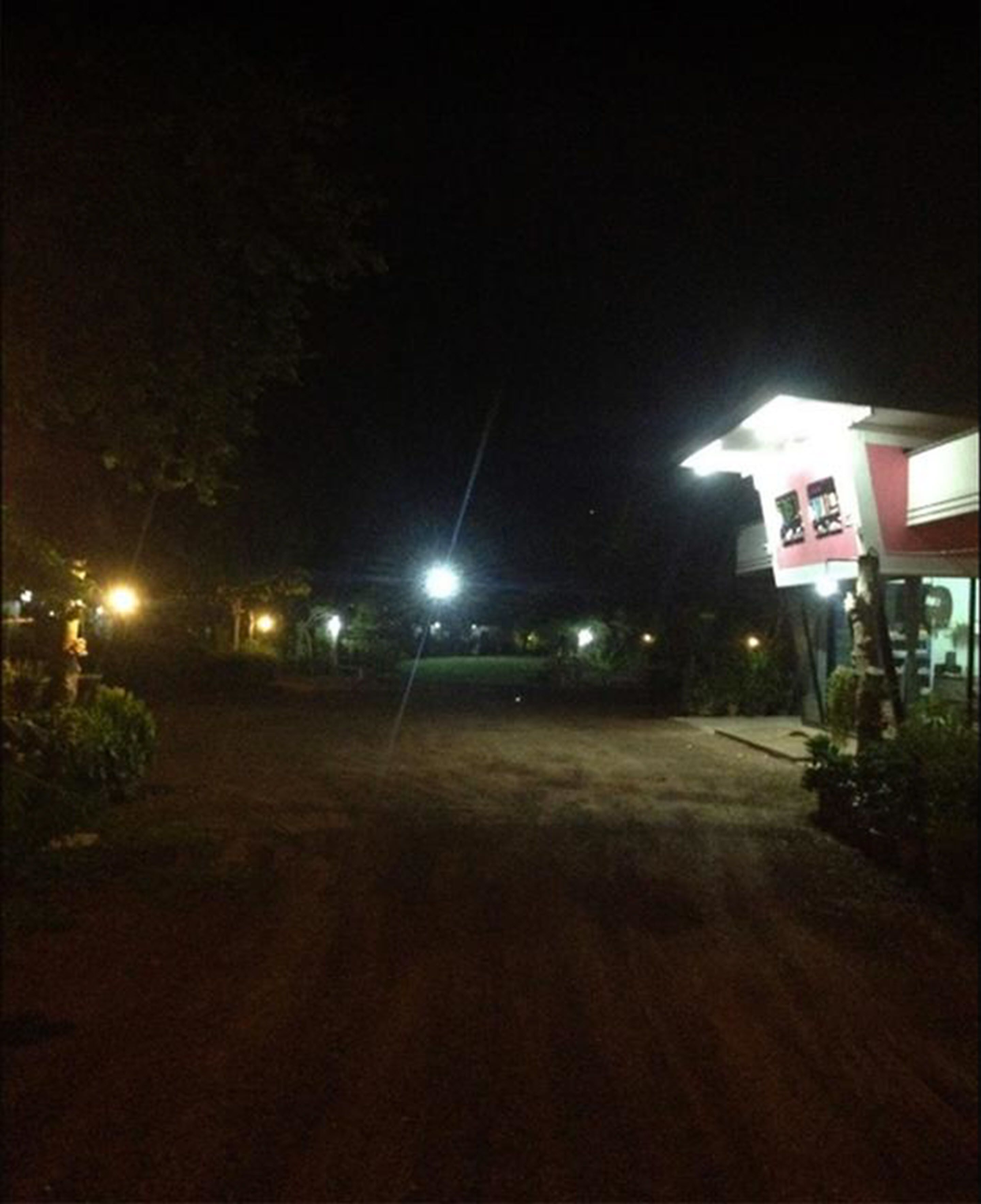 Vista nocturna de un camino de tierra que conduce a un edificio con un letrero luminoso.