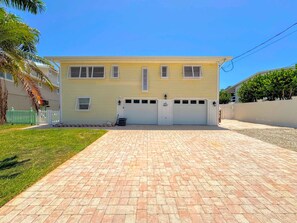 A two-story house with a garage, a paved driveway, and a white picket fence. - 390 Bayland Canalfront Pool Home by Beach (Fort Myers Beach)