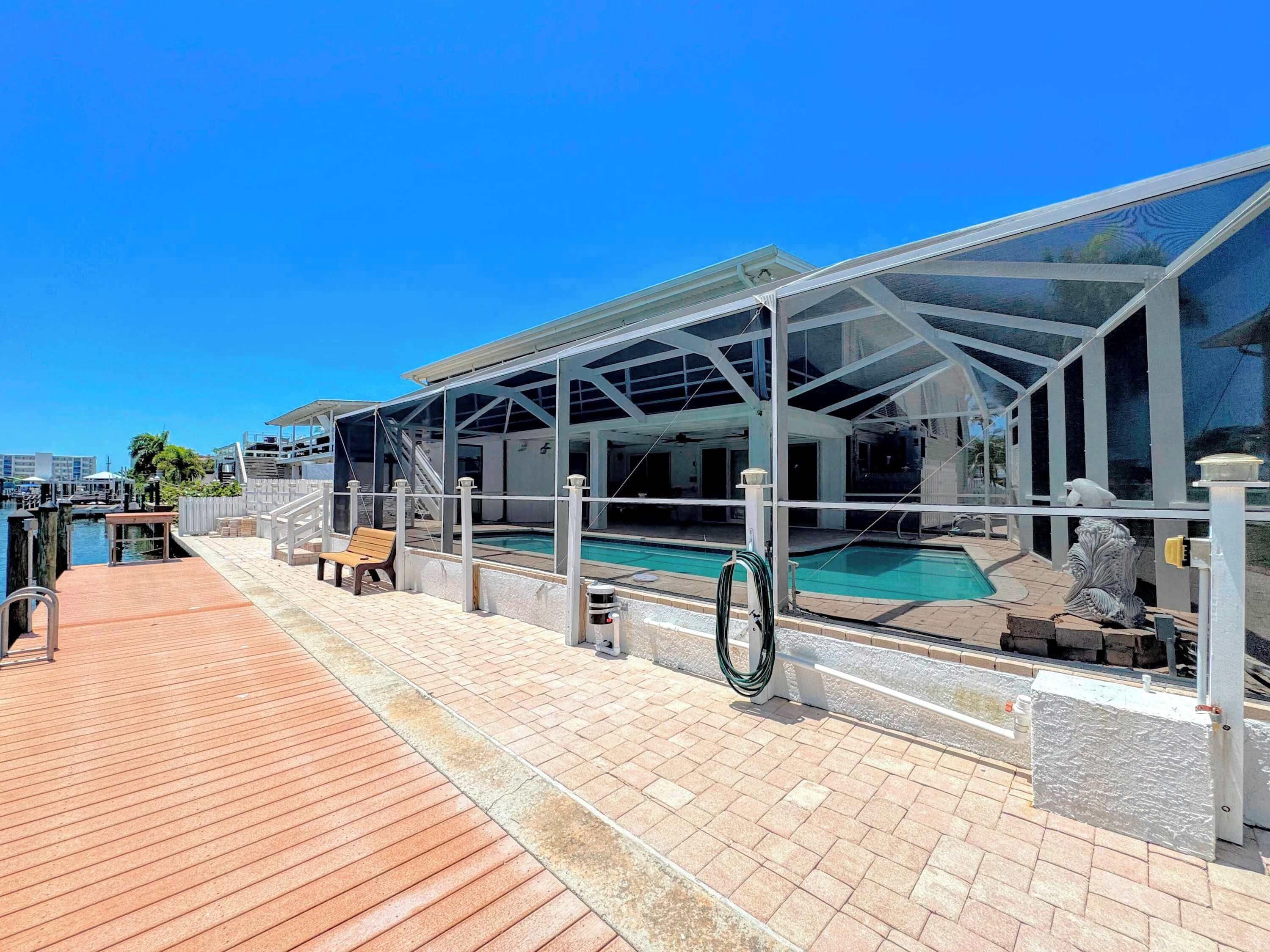 A covered outdoor swimming pool with a glass enclosure, a wooden deck, and a view of the marina.