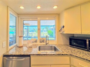 A kitchen with a granite countertop, stainless steel sink, and a microwave. - 390 Bayland Canalfront Pool Home by Beach (Fort Myers Beach)