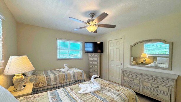 Habitación de hotel con dos camas, ventilador de techo, televisor, cómoda y espejo.