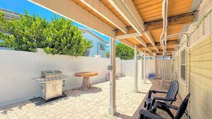 Un patio exterior con una parrilla, una mesa de madera y sillas negras.