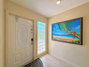 A hallway with a white door, a window with a view of the beach, and a painting of parrots on a tree. - 390 Bayland Canalfront Pool Home by Beach (Fort Myers Beach)