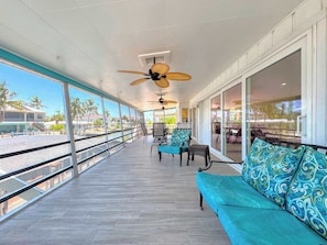 A covered outdoor area with a seating arrangement, large windows, and ceiling fans.