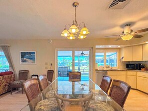 A dining area with a glass table surrounded by wicker chairs, a ceiling fan, and a view of the outdoors.