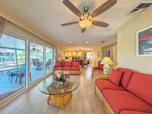 A spacious living area with a glass coffee table, red sofas, and a ceiling fan. - 390 Bayland Canalfront Pool Home by Beach (Fort Myers Beach)