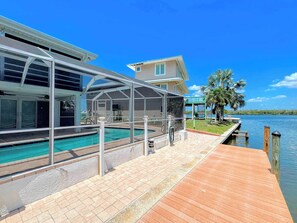 A waterfront property with a swimming pool, covered patio, and a wooden dock extending into the water.