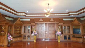 A spacious room with wooden paneling, a large wooden door, and two vases with flowers. - Rai Fhun Pen Jing Resort (Sung Noen)