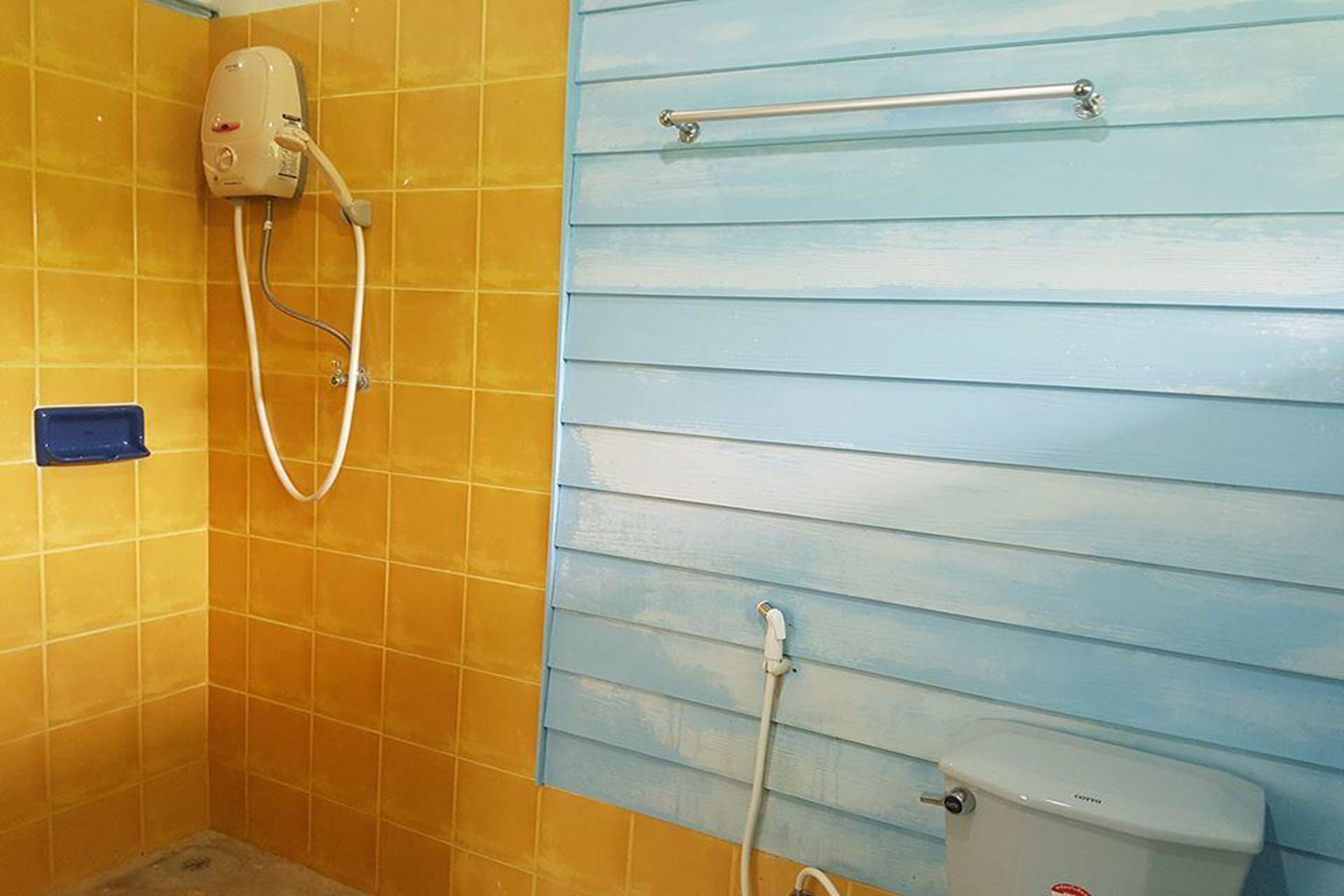 Un baño con paredes de azulejos amarillos, una cabina de ducha azul y un inodoro blanco.