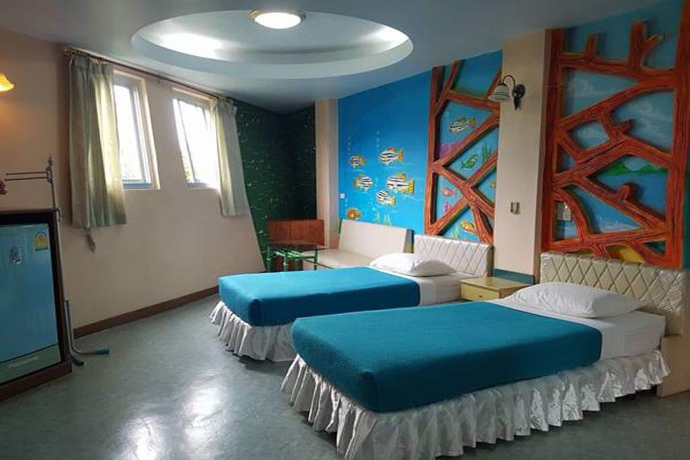 A room with two beds, a desk, a chair, and a wall mural.