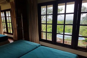 Una habitación con dos camas, una ventana que da a zonas verdes y una cortina.