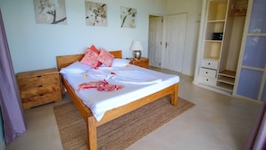 A bedroom with a wooden bed, a nightstand, a bedside table, a lamp, and a wardrobe. - Kaz Bulinger (Mahé Island)