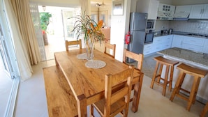 A wooden dining table with chairs, a kitchen with white cabinets, and a view of the outside. - Kaz Bulinger (Mahé Island)