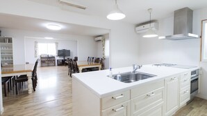Een moderne keuken met witte kastjes, een groot eiland met een spoelbak, en een eethoek met houten stoelen en een tafel.
