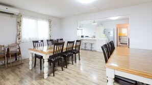 Een ruime eethoek met een houten tafel en stoelen, een keuken op de achtergrond, en een heldere plafondlamp.
