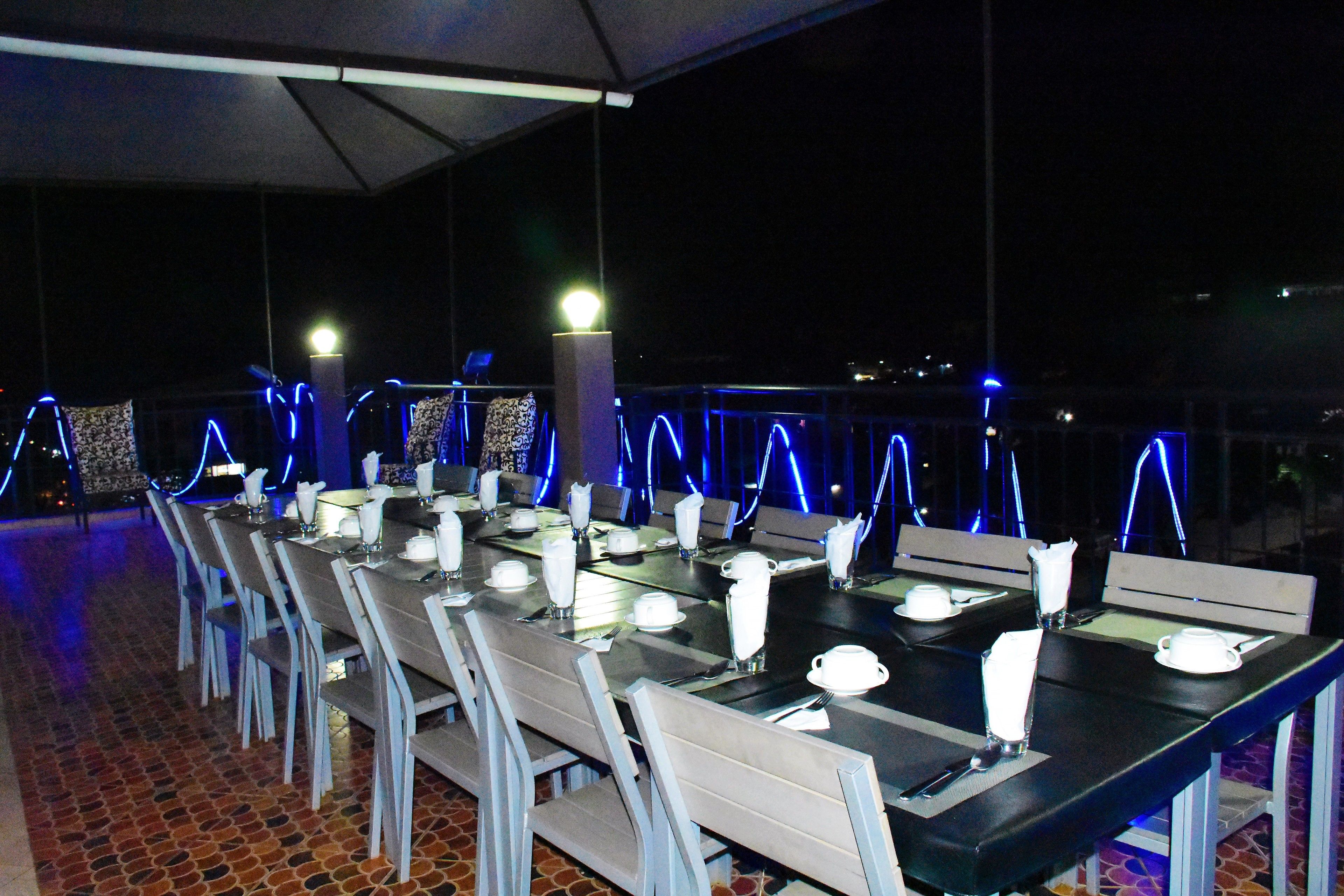 A restaurant with tables set for dining, outdoor seating, and blue ambient lighting.