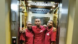 Tres personas con camisetas rojas de pie dentro de un ascensor.