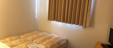 Una habitación de hotel con una cama, un escritorio con computadora y una ventana con cortinas.