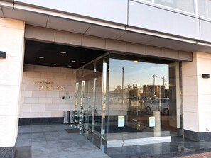 Une entrée moderne avec des portes vitrées, un sol carrelé et une vue dégagée sur les voitures garées à l’extérieur.
