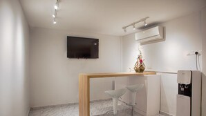 A modern kitchen with a wooden countertop, two bar stools, a water dispenser, and a flat-screen TV mounted on the wall. - The Marion Hotel (Johor Bahru)