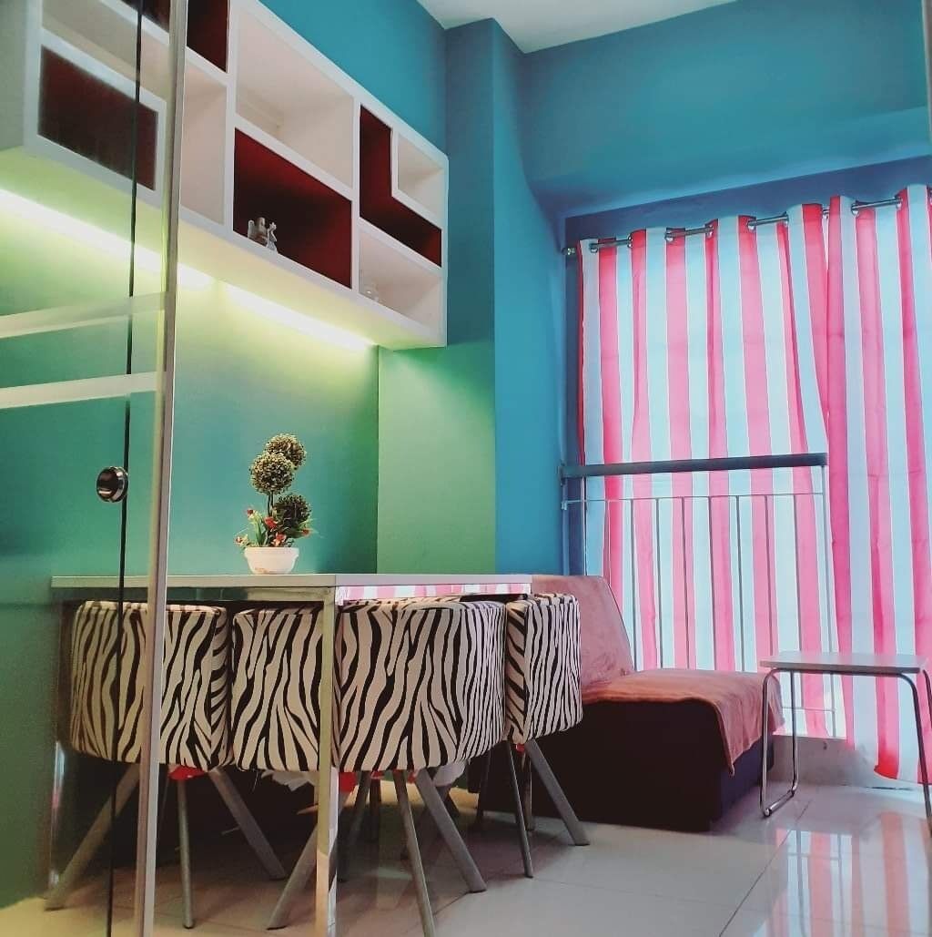 Una habitación con paredes verde agua, una mesa a rayas de cebra, una pequeña planta en maceta y una cortina a rayas.