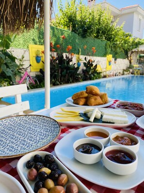 A poolside breakfast setup with a table, plates of food, and a pool in the background.