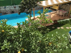 A pool area with a table and chairs, surrounded by greenery and a stone wall.
