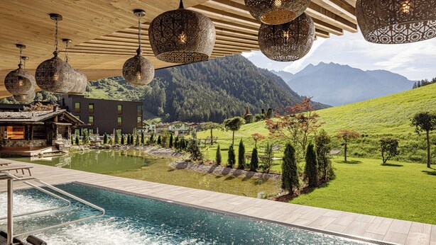 Un espace piscine offrant une vue sur les montagnes, une terrasse en bois et des lampes suspendues.