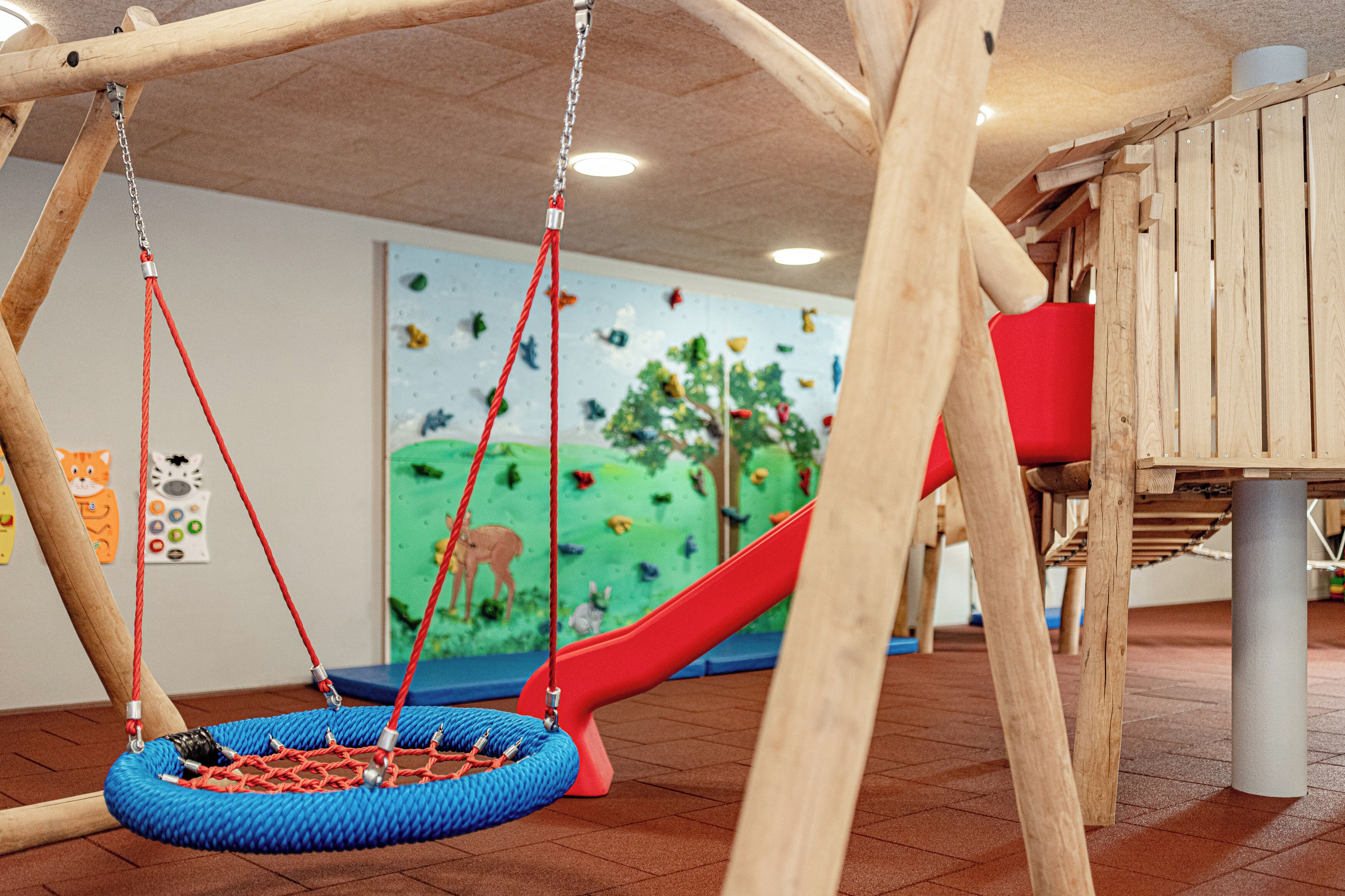 Zona infantil con columpios, tobogán y pared de escalada.