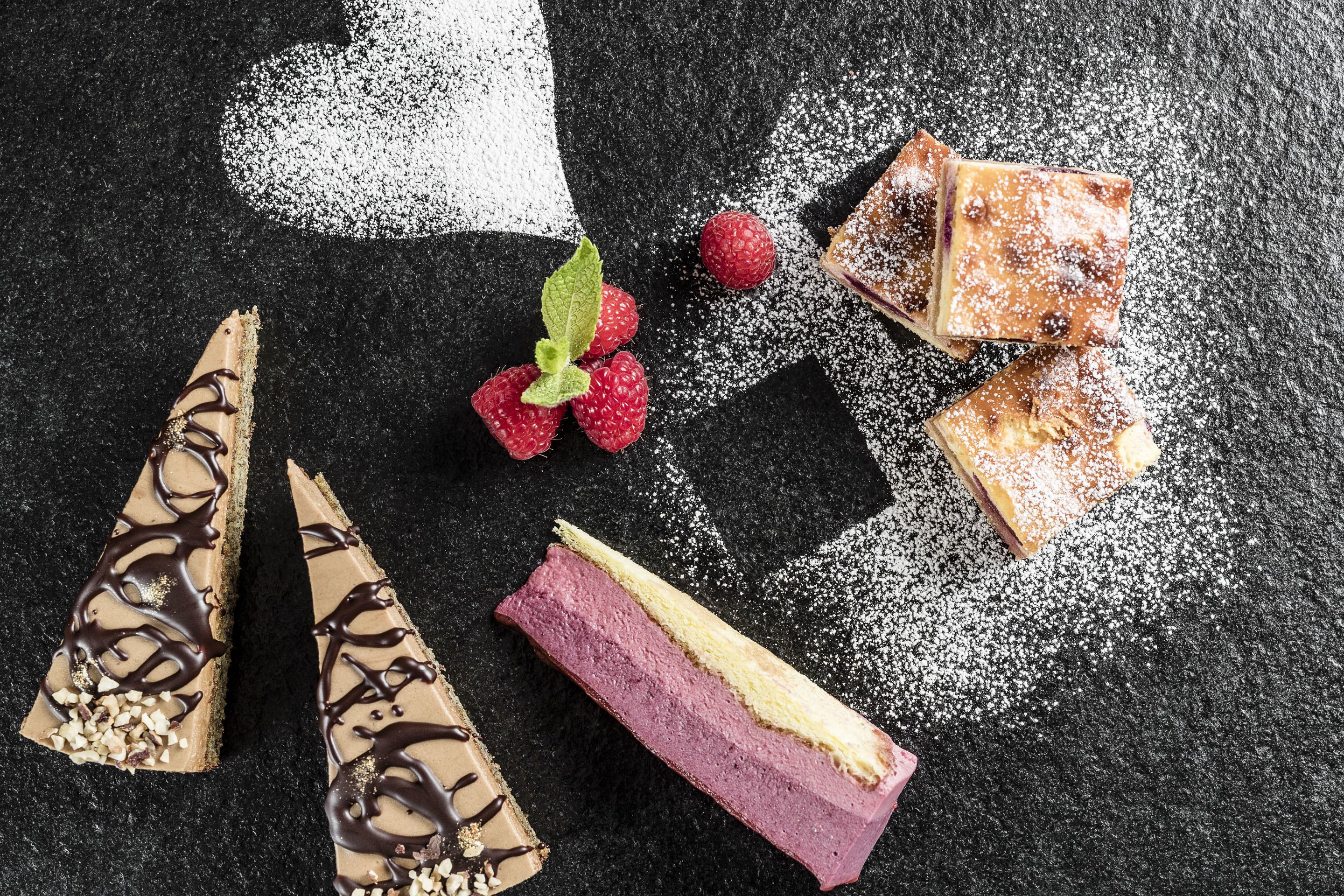 Un arreglo de postres con diversos pasteles y frutas sobre una superficie oscura.