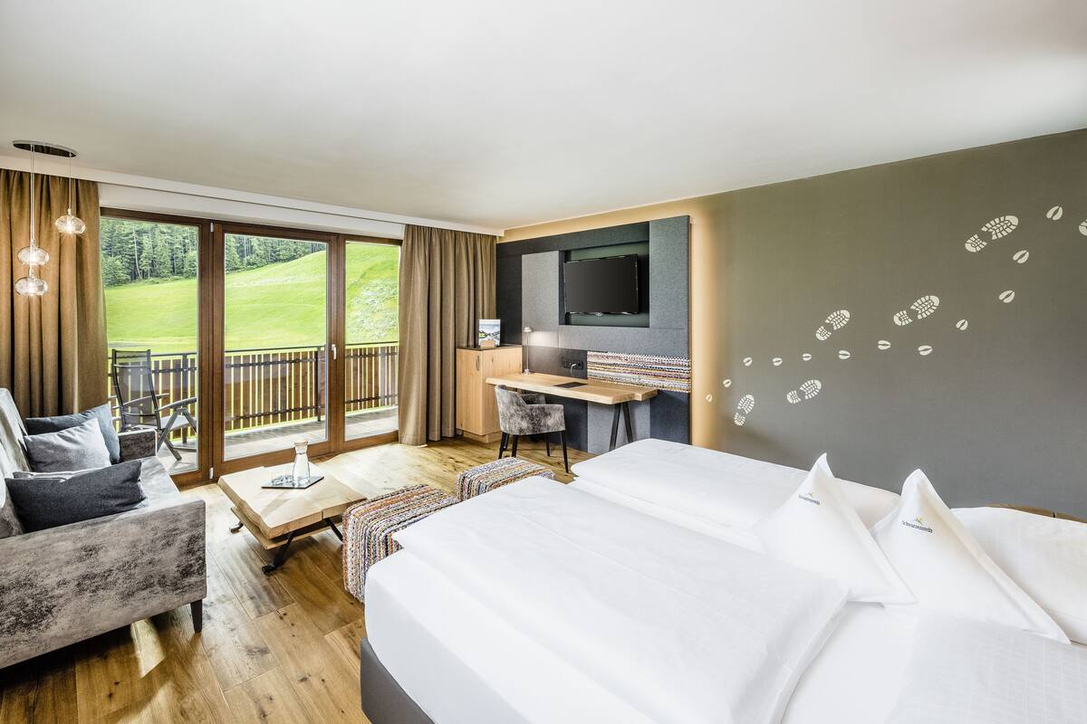 A hotel room with a large bed, a desk, a chair, and a balcony with a view of the outdoors.