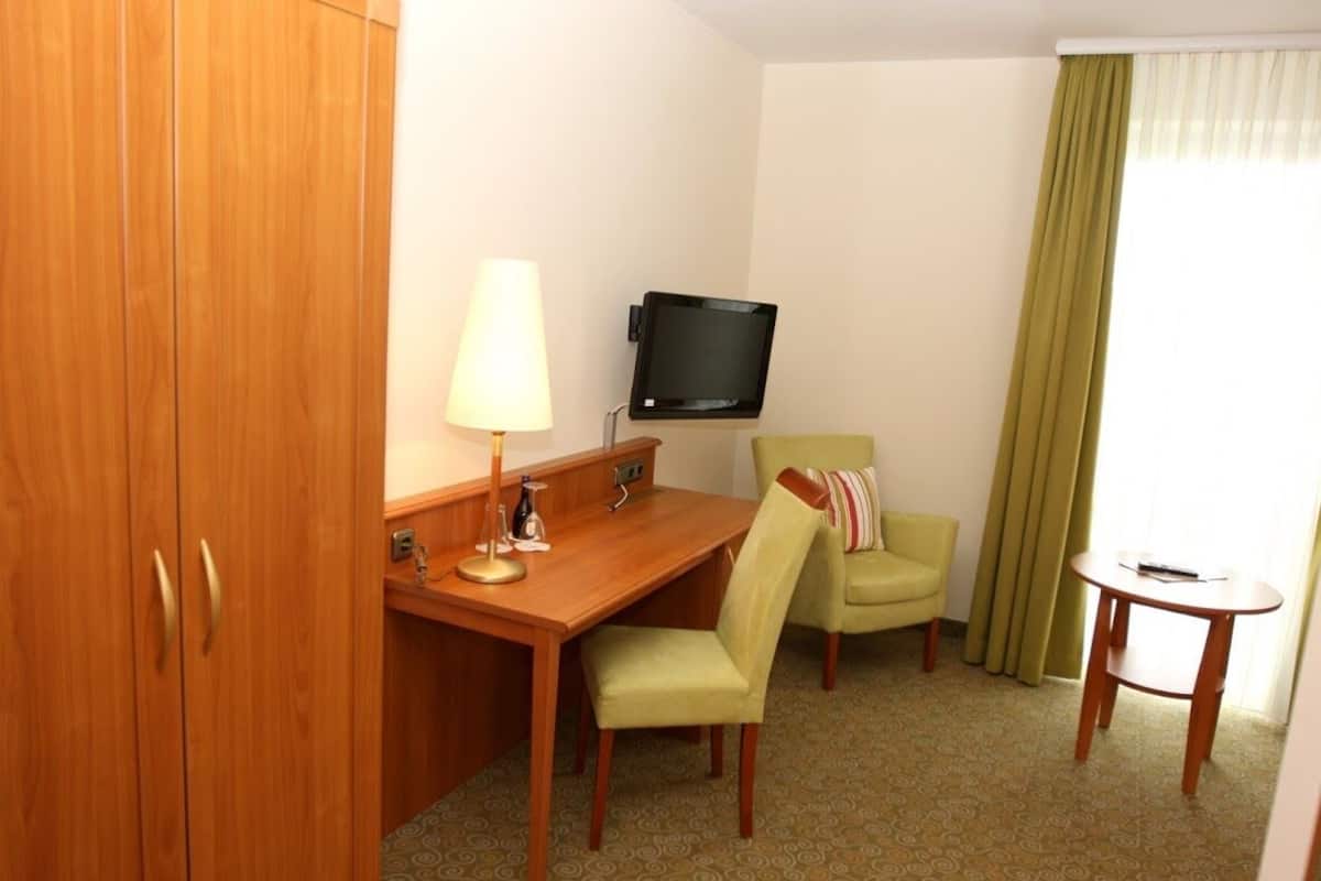 Une chambre d’hôtel avec un bureau en bois, une télévision, un fauteuil vert et une petite table.