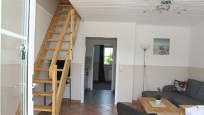 Una sala de estar con una escalera de madera, un sofá gris, una mesita de centro y vista a la cocina.
