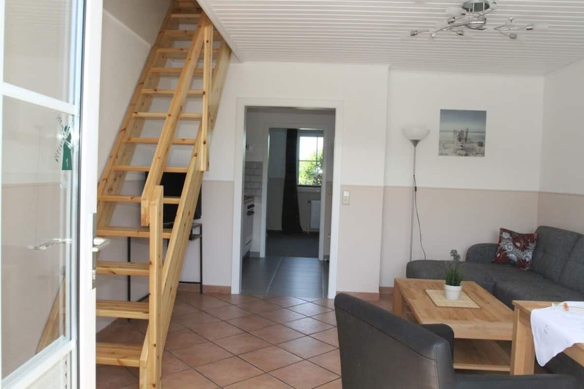 Un salon avec un escalier en bois, un canapé gris, une table basse et une vue sur la cuisine.