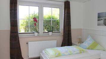 Een slaapkamer met een bed, een raam met gordijnen, een radiator en een nachtkastje met een lamp.