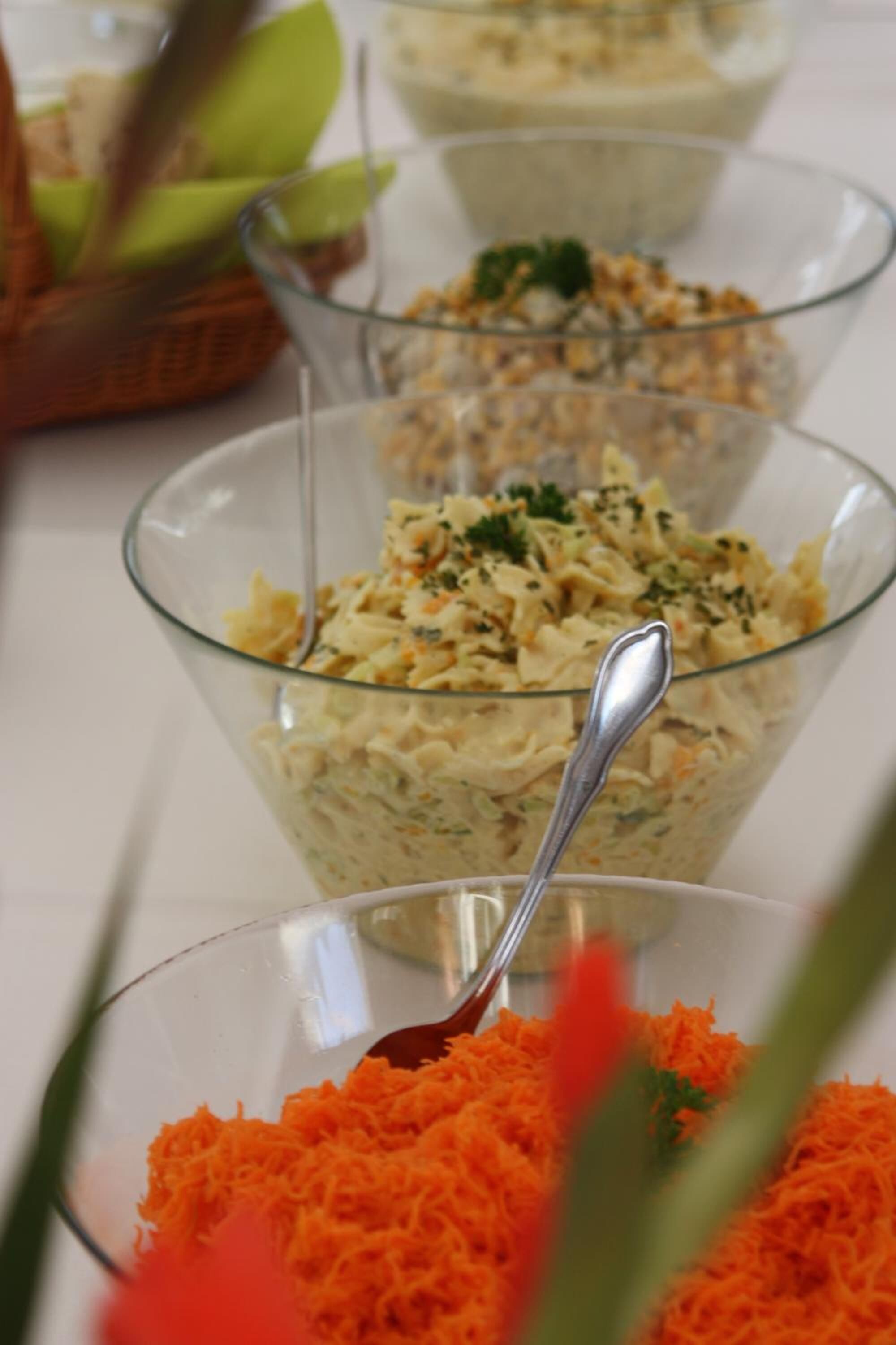 A series of glass bowls containing a creamy salad with shredded carrots, garnished with herbs.
