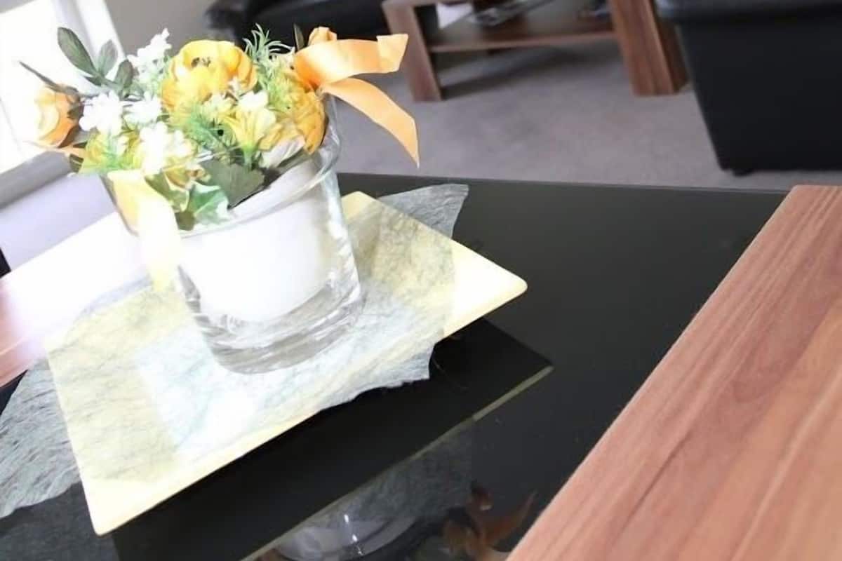 Un salon avec un canapé noir, une table basse en bois et un vase de fleurs posé sur une table.