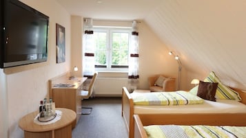 A bedroom with a bed, a desk, a chair, a TV, and a window with curtains.