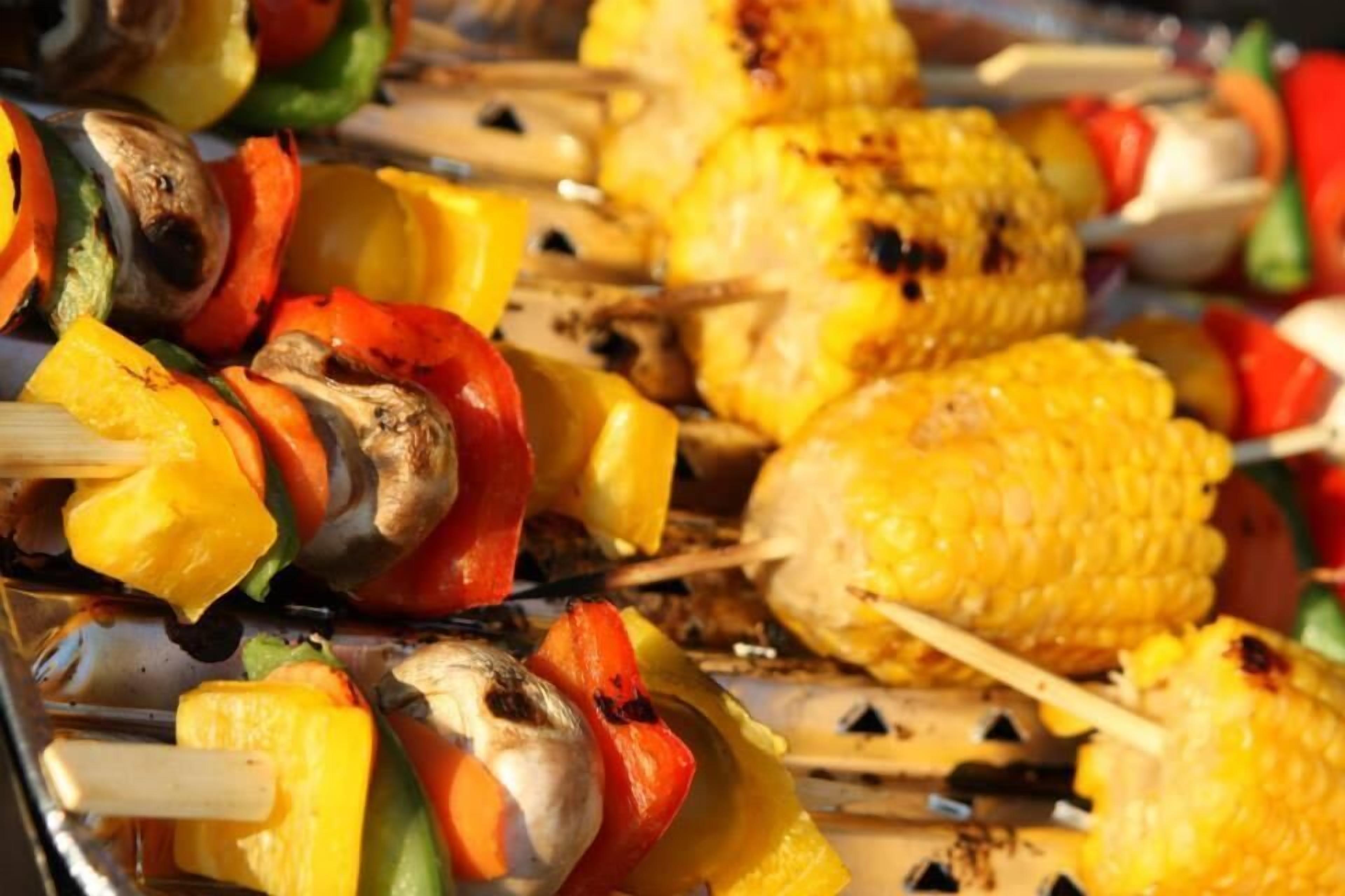A variety of grilled vegetables and corn on skewers.