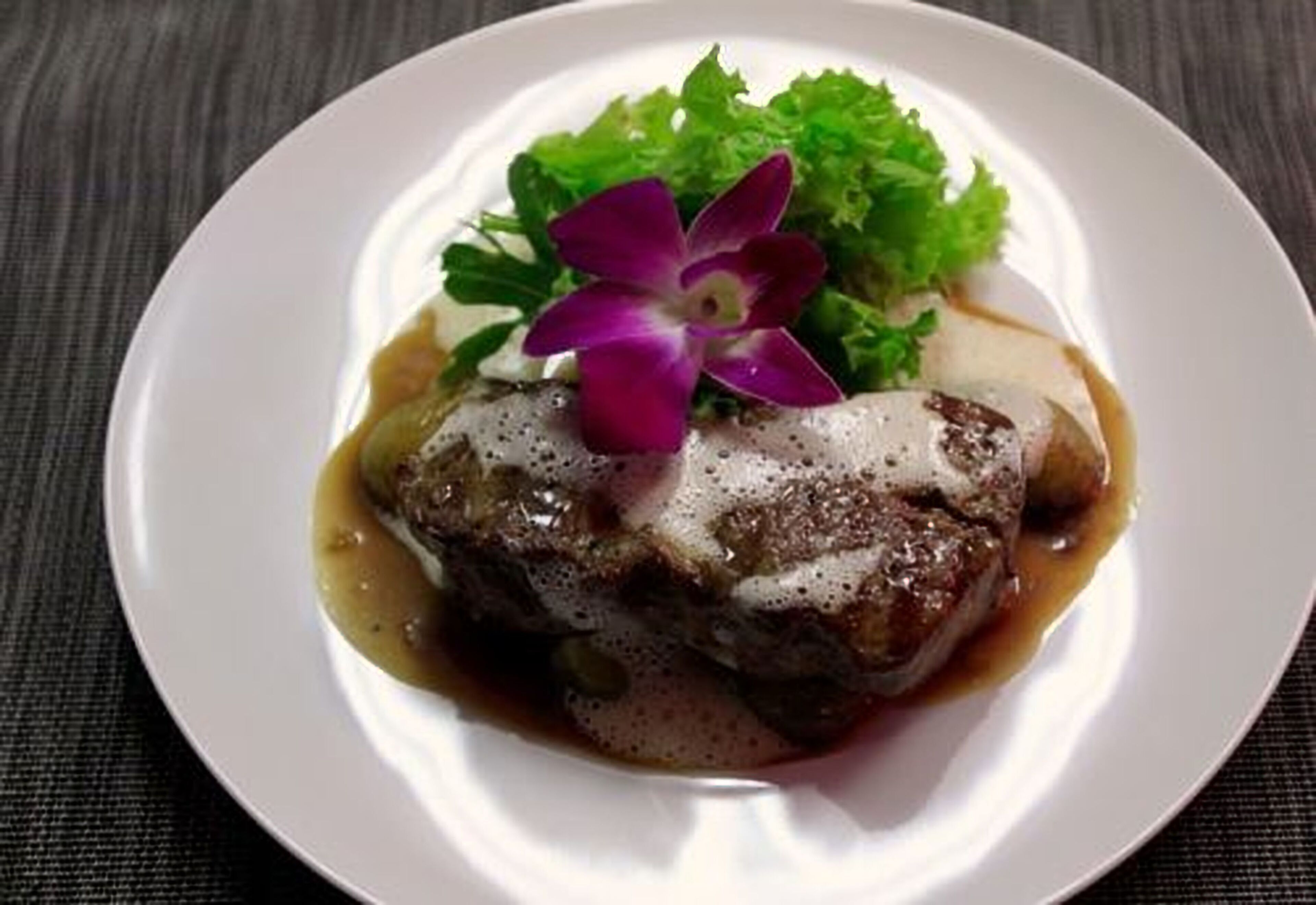 Un plato con guiso de carne, salsa y una flor púrpura como adorno.