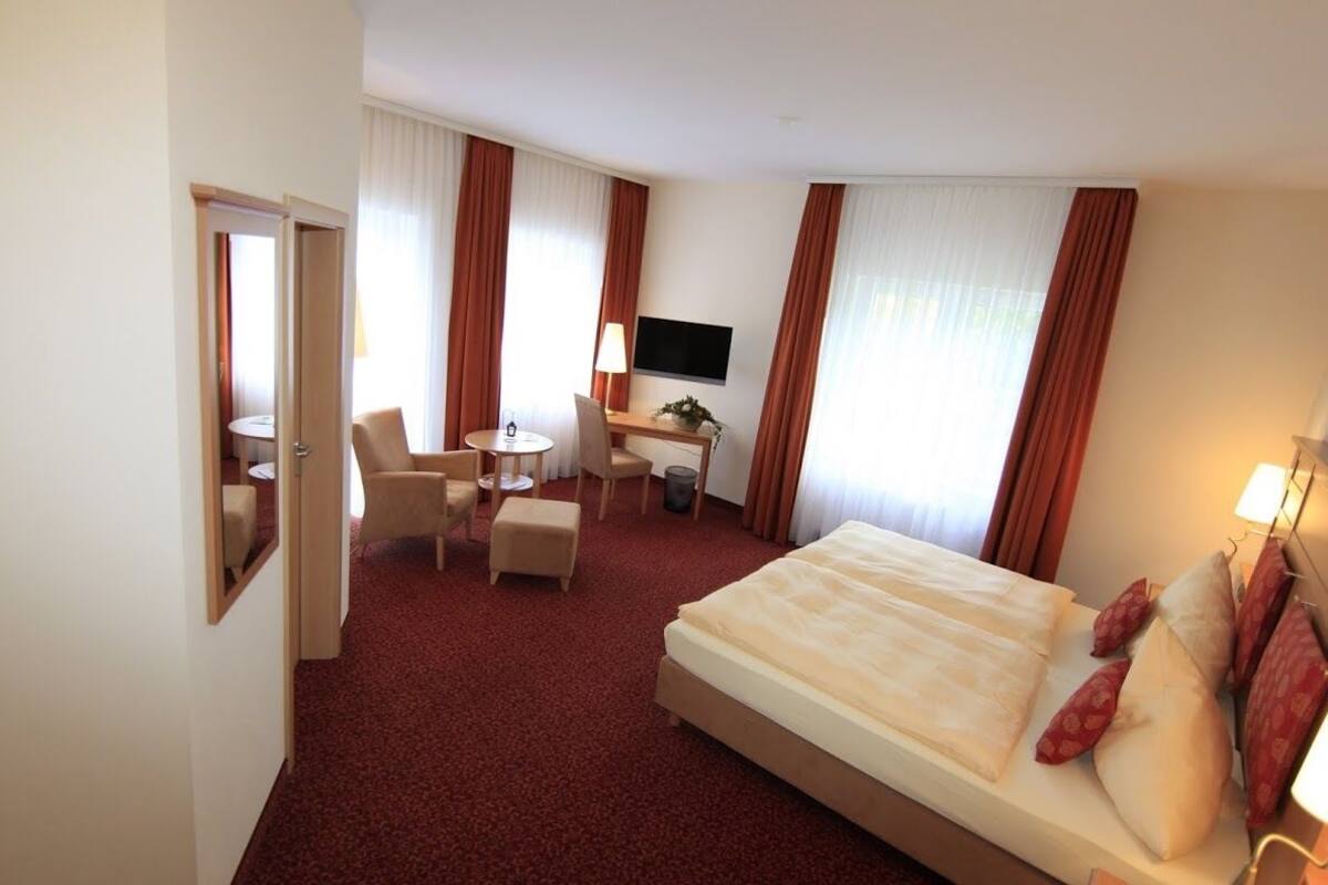 Une chambre d’hôtel avec un grand lit, un bureau avec une chaise, une petite table et un téléviseur fixé au mur.