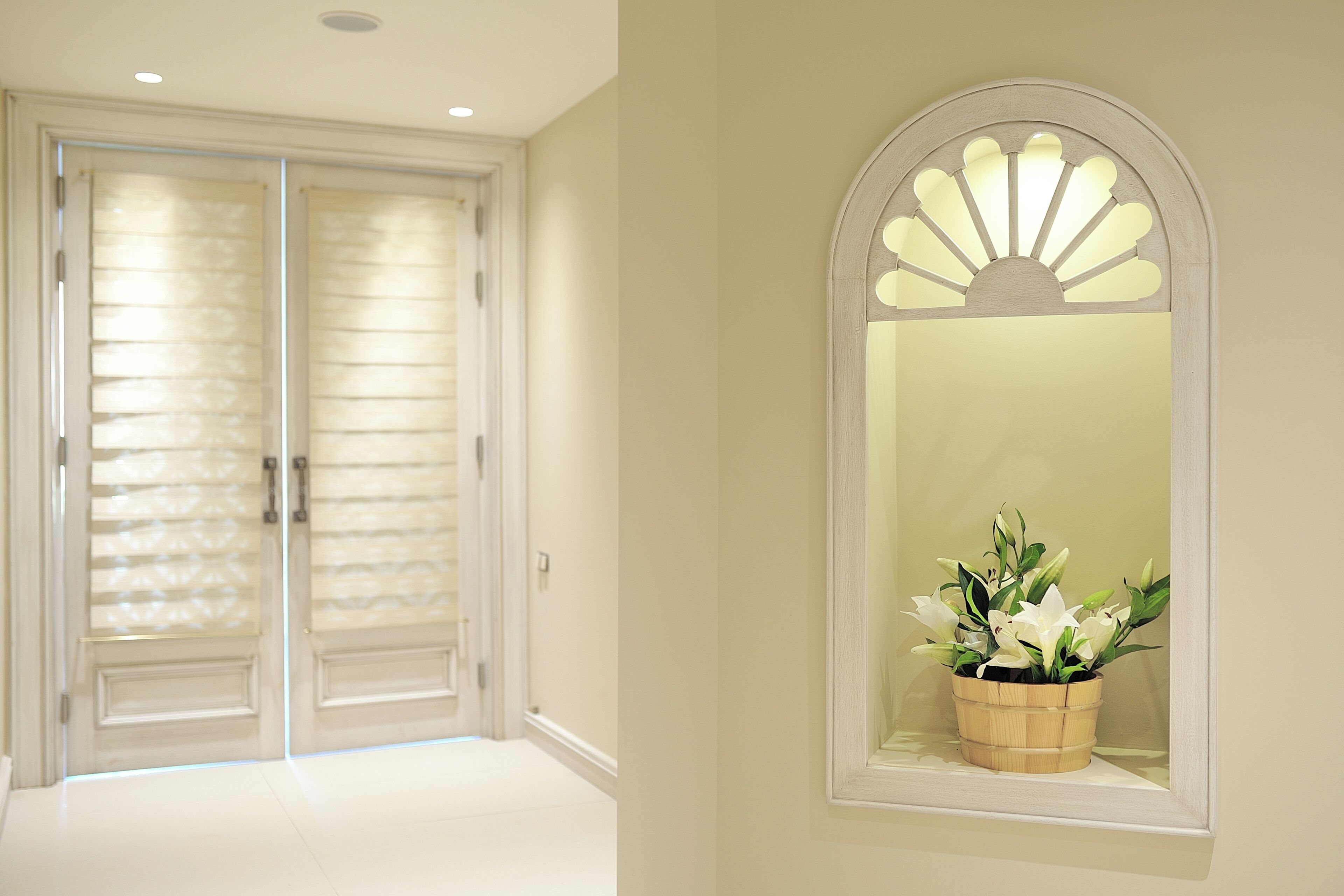 A hallway with a double door, a wooden-framed window with a plant, and a wall-mounted light fixture.