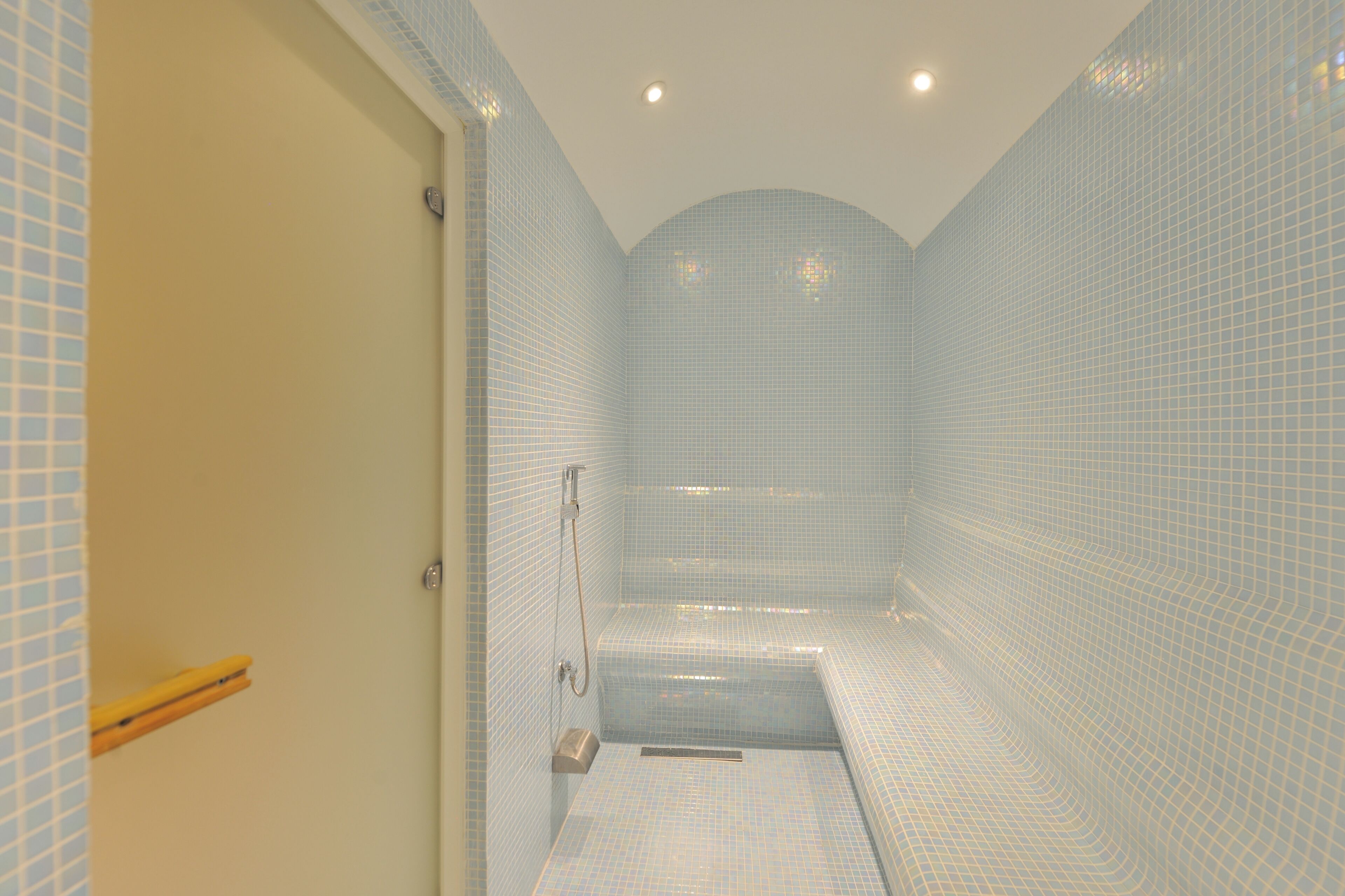 A bathroom with a tiled wall, a shower area, and a door with a towel rack.