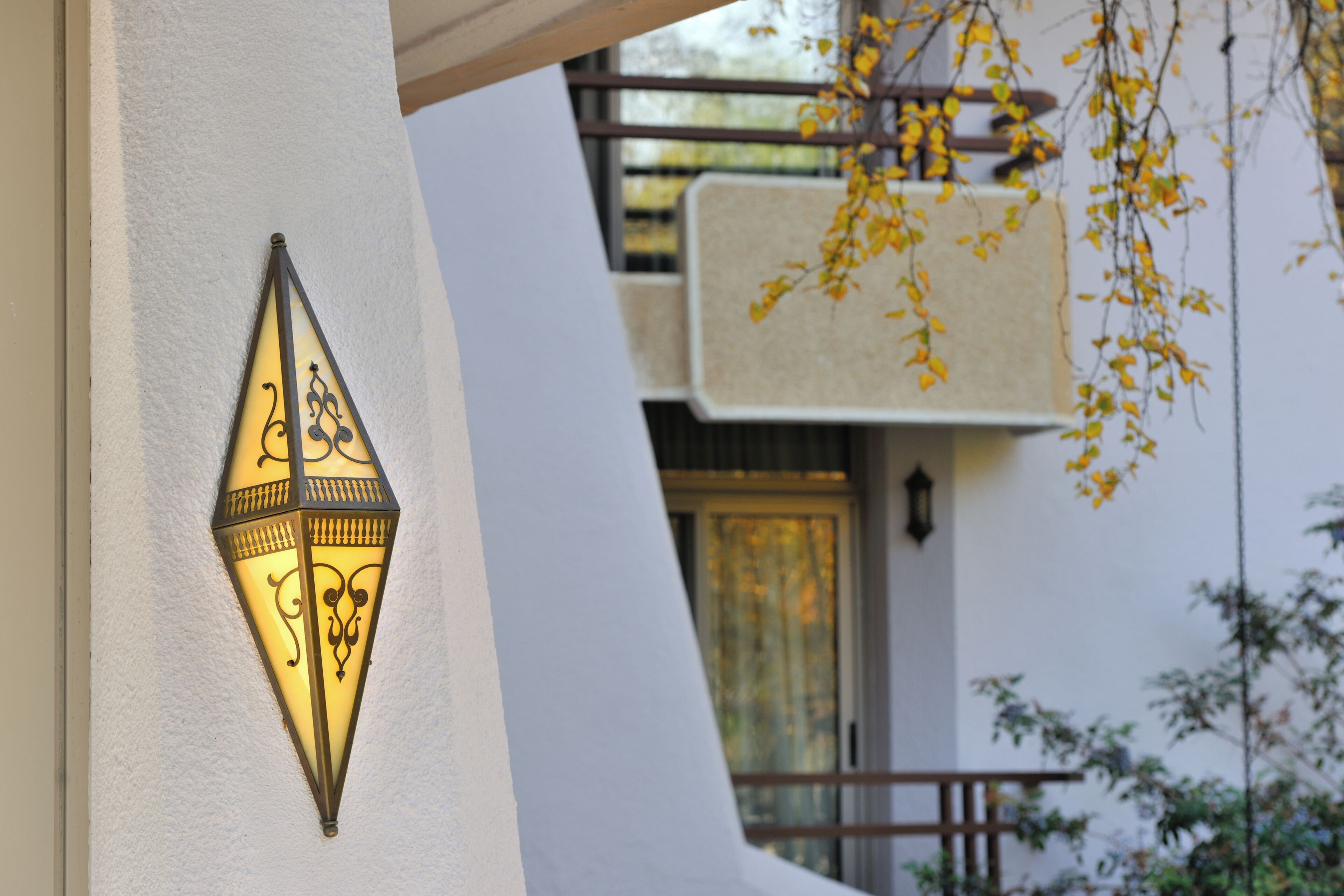 A wall-mounted light fixture with intricate designs, a white wall, and a window with a curtain.
