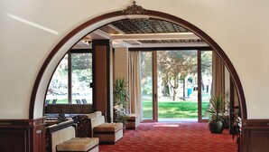 A hotel lobby with a red carpet, a seating area with sofas and a bench, a large arched doorway, and potted plants. - Agacli Hotel (Aksaray)