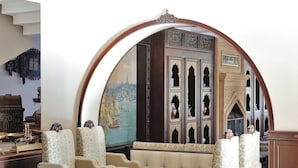 A room with a large arched mirror, a sofa set, a decorative cabinet, and a painting of a cityscape. - Agacli Hotel (Aksaray)
