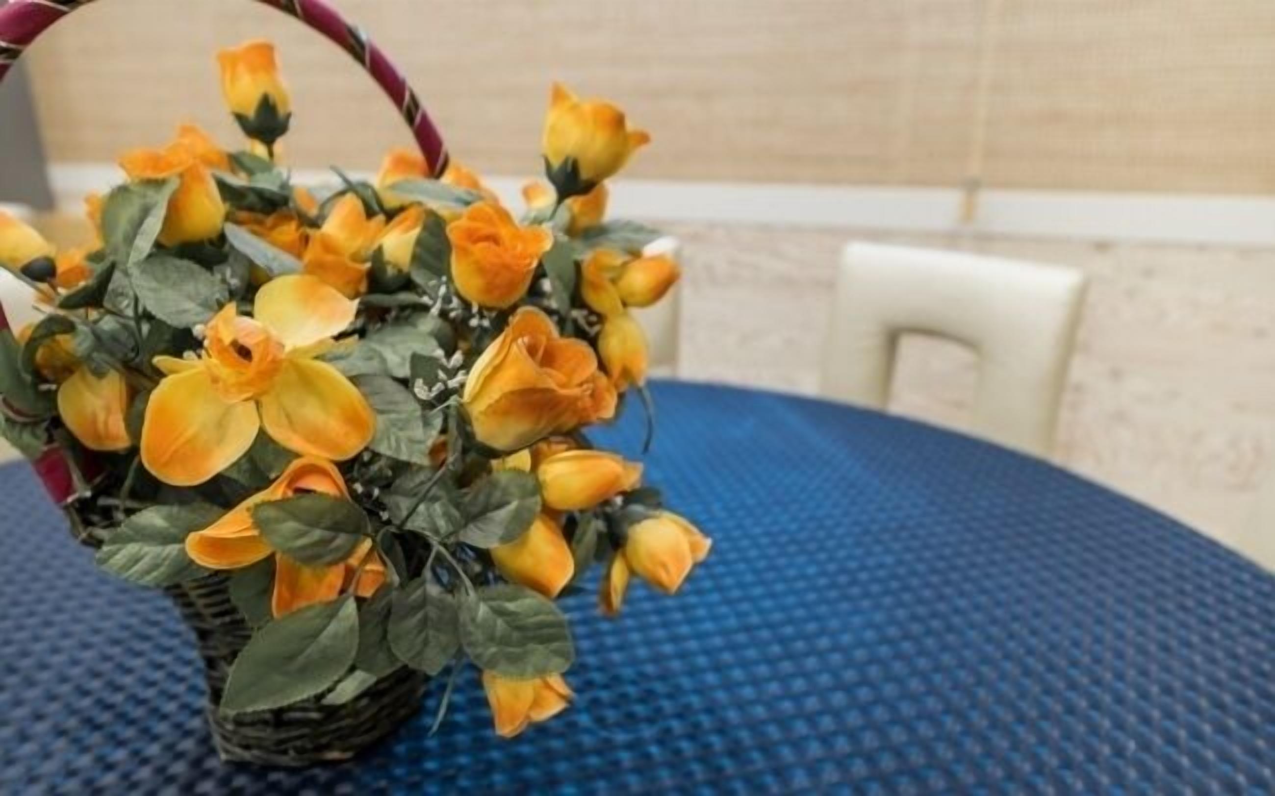 A wicker basket with yellow flowers on a blue textured table.