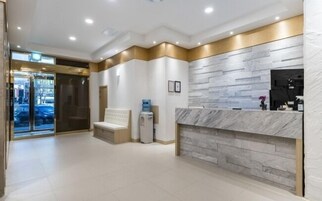 Uma área de recepção de hotel com balcão de mármore, um banco e um bebedouro.